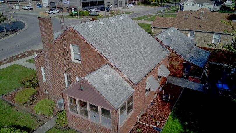 Before roof replacement: gray shingle roof on a brick home.